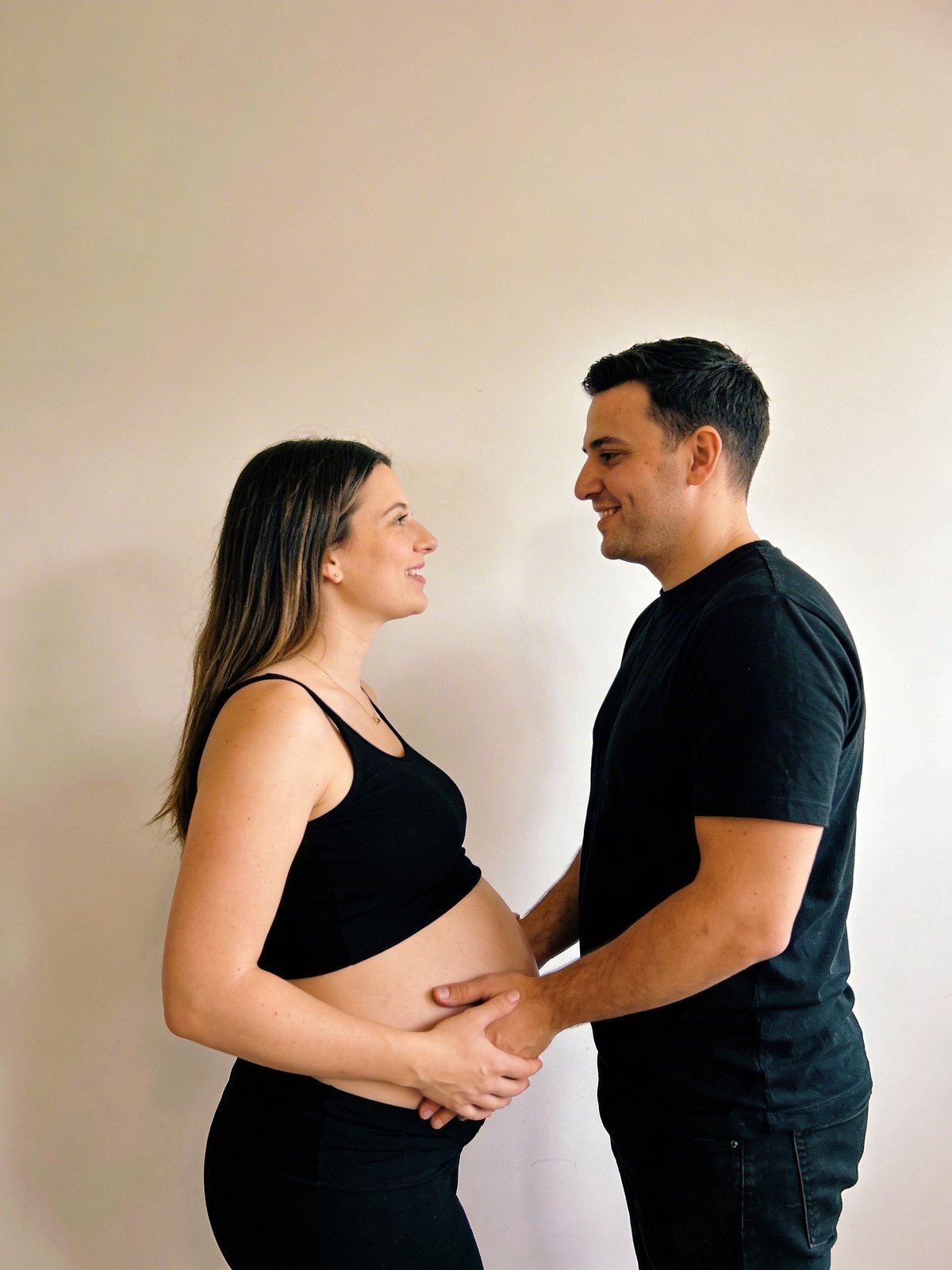 Pareja de futuros padres con ropa coordinada, cara a cara con las manos sobre la barriga