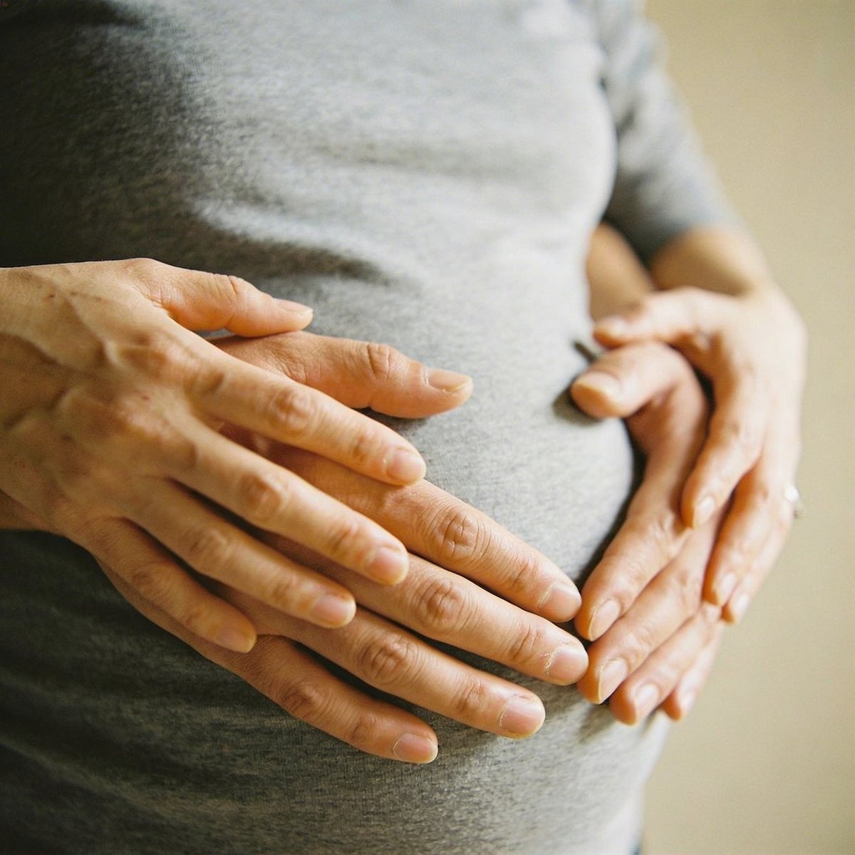 Primer plano de las manos de la futura mamá y el papá formando un corazón sobre la barriga redonda